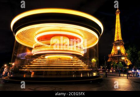 Helle Lichtspuren auf dem sich drehenden Karussell in der Nähe des prächtigen Eiffelturms bei Nacht in Paris, Frankreich. Stockfoto