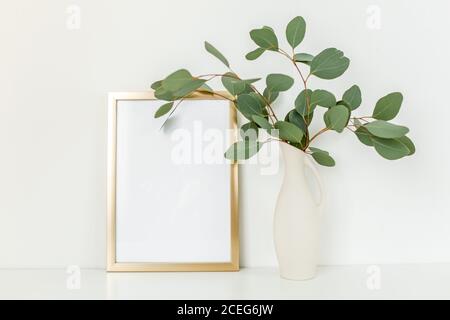 Blanker Rahmen Mockup mit einem Zweige von Eukalyptus in Vase auf Tisch auf hellem Hintergrund. Inneneinrichtung. Blog, Website oder Social Media Konzept. Stockfoto