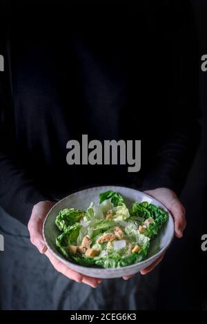 Crop reife Frau in dunklen Kleidern halten Schüssel mit leckeren Salat. Stockfoto