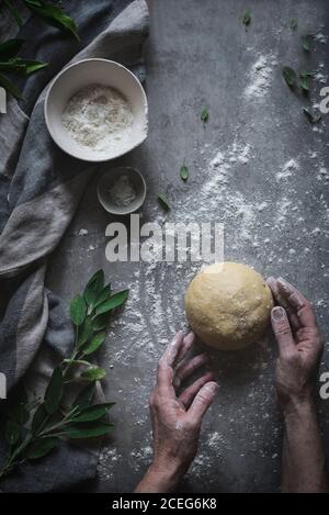 Crop Schuss von oben von Senior Person kneten Ball Weicher Teig auf Marmortheke mit Mehl bestreut Stockfoto