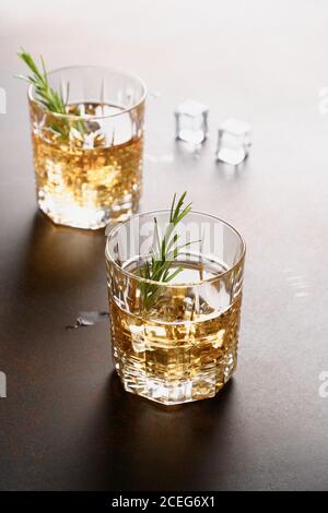 Zwei Gläser kalter Whiskey mit Rosmarin-Zweig auf dunkelbraunem Hintergrund. Vertikal. Stockfoto