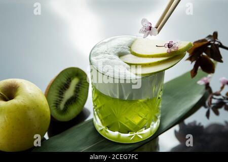 Kristallglas mit servierten Getränken in grüner Farbe serviert mit apfelscheiben und kleine Blumen auf dem Tisch mit grünen Früchten Stockfoto