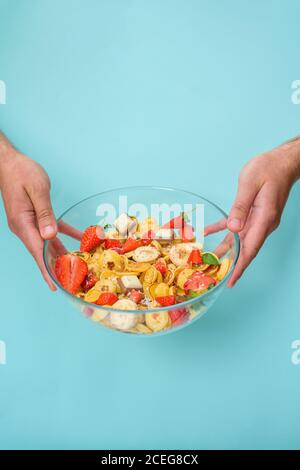 Winzige Pfannkuchenschüssel Müsli mit frischen Erdbeeren, Banane, Schokolade, Kokosraspeln und Honig in Untertasse auf blauem Hintergrund. Die Tendenz zu selbst-i Stockfoto