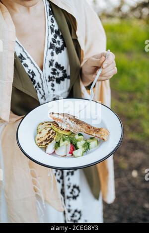 Gesichtslose Aufnahme einer Frau mit frischem Gemüse mit gegrilltem Lachsfilet und Zucchini beim Picknick Stockfoto