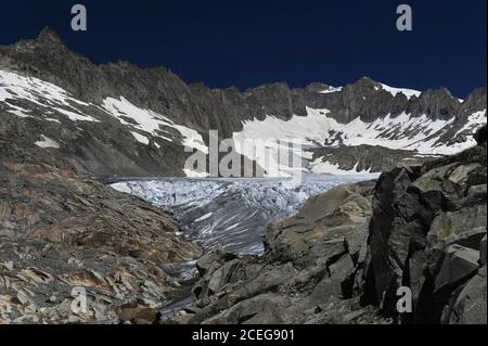 Zerklüftete Urner Alpen Gipfel des Dammastock und Tieralplistocks bilden eine Naturarena und eine spektakuläre Sommerkulisse auf der tief gespalten Oberfläche des 7.65 km (4.75 mi) großen Gletschers, der auf etwa 30 bis 40 m (100 bis 130 ft) fließt. Pro Jahr von hohen Schneefeldern bis zu einem Punkt unterhalb des Furka-Passes auf einer Höhe von etwa 2,208 m (7,244 ft). Das Schmelzwasser bildet einen See, von dem aus ein Bach in das darunter liegende Tal stürzt, um die 813 km (505 mi) lange Fahrt des Flusses Rhône über Südfrankreich und das Camargue-Delta ins Mittelmeer zu beginnen. Stockfoto