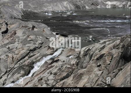 Klimaforscher beschuldigen den zurückziehenden Rhône-Gletscher, die Quelle des Flusses Rhône, der im Sommer unterhalb des Furka-Passes im Kanton Wallis in der Schweiz auf einer Höhe von etwa 2,208 m (7,244 ft) schmilzt. Im Jahr 1850 dehnte sich eine Eiszunge weit unten am Berg aus, bevor sie im Tal darunter schmolz. Der Gletscher fließt über 7.65 km (4.75 Meilen) von hohen Urner Alpen Schneefeldern auf etwa 30 bis 40 m (100 bis 130 ft) pro Jahr. Der Strom, der aus dem Schmelzwassersee fließt, beginnt die 813 km (505 Meilen) lange Reise des Flusses durch Südfrankreich zum Mittelmeer. Stockfoto