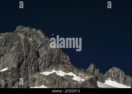 Ein eingleisiger Gleitschirm fährt in einem tiefblauen Himmel, nachdem er die zerklüftete Oberfläche eines zackigen Bergrückens in den Urner Alpen hoch im Kanton Wallis, Schweiz, hoch über dem 7.65 km (4.75 mi) großen Gletscher abrutscht. Das Gletschereis schmilzt auf einer Höhe von etwa 2,208 m oder 7,244 Fuß, wobei das Schmelzwasser in ein tiefes Talbecken stürzt, weit unten, um die 813 km (505 Meilen) lange Reise des Flusses Rhône zum Mittelmeer über Südfrankreich und das Camargue-Delta zu beginnen. Stockfoto