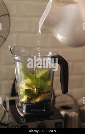 Gießen Sie Wasser aus Keramik Krug in Kunststoff Tasse Mixer Gefüllt mit Obst und Gemüse Mischung für Smoothie Stockfoto
