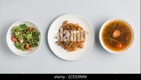 Schöne Schüsseln mit Miso-Suppe und frischem Gemüse Salat und Teller mit Sushi-Brötchen und Holzstäbchen liegen Auf weißem Hintergrund von oben Stockfoto