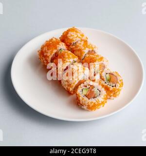 Helle leckere japanische Sushi-Brötchen mit Lachs in fliegenden Fischen Kaviar wunderschön auf weißem Teller auf weißem Hintergrund von gesetzt Oben Stockfoto