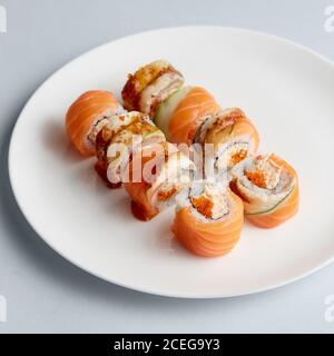 Helle leckere japanische Sushi-Brötchen mit Lachs in fliegenden Fischen Kaviar wunderschön auf weißem Teller auf weißem Hintergrund von gesetzt Oben Stockfoto