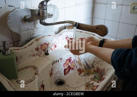 Ernte weibliche Reinigung Hände unter läuft aus Metall Wasserhahn Wasser In alten geknackten weißen Waschbecken mit floralen Ornamenten Stockfoto