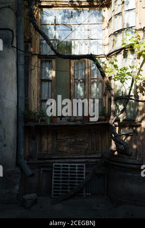 Blick im Freien auf alte offene Holzfenster mit schmalen Flügel Mit verwitterten Holzplankenwänden und Töpfen mit Pflanzen stehen Auf geschwungener abgenutzter Schwelle bei Tageslicht Stockfoto