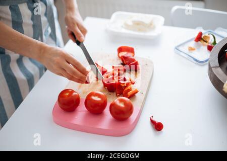 Ernte Ansicht von?Frau in Sommerkleidung Schneiden helle leckere frische Tomaten auf Holzbrett mit anderen Zutaten Kochen auf dem Tisch in der Nähe liegen Stockfoto