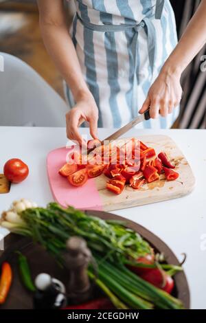 Ernte Ansicht von?Frau in Sommerkleidung Schneiden helle leckere frische Tomaten auf Holzbrett mit anderen Zutaten Kochen auf dem Tisch in der Nähe liegen Stockfoto