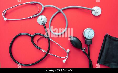 Blutdruckmessgeräte, Hypertonie-Kontrolle. Medizinische Stethoskope und Sphygmomanometer auf rotem Hintergrund, Draufsicht. Stockfoto