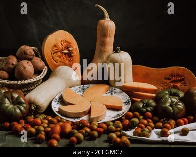 Schöne warme Anordnung von reifen Butternut Squashes auf Tisch mit Winzige Tomaten und Teller mit Scheiben Stockfoto