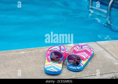 chevron-Muster auf Flip-Flops am Swimmingpool mit Sonnenbrille Stockfoto