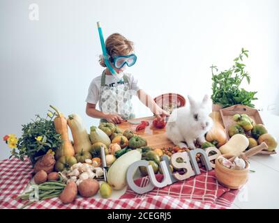 Kleiner Junge stehend und Kochen Gemüse am Tisch mit liebenswert Weißes Kaninchen Stockfoto