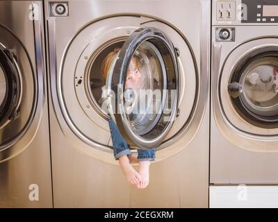 Liebenswert neugierigen Jungen sitzt in der Waschmaschine in der Wäsche. Stockfoto