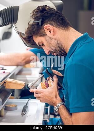 Schöner Mann in Uniform Schnitzen Zähne auf Prothese während der Arbeit im Dentallabor. Stockfoto