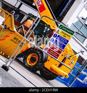 Gabelstapler Baumaschinen und Müll überspringt mit Gesundheit und Sicherheitshinweise hinter EINEM Sicherheitszaun Stockfoto