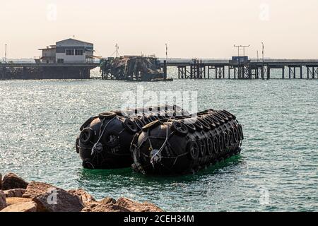 Riesige Bojen, die in Autoreifen eingewickelt sind, schweben im Hafen von Darwin, Northern Territory, Australien, mit einem langen Holzsteg und Gebäuden, die sich dahinter erstrecken. Stockfoto