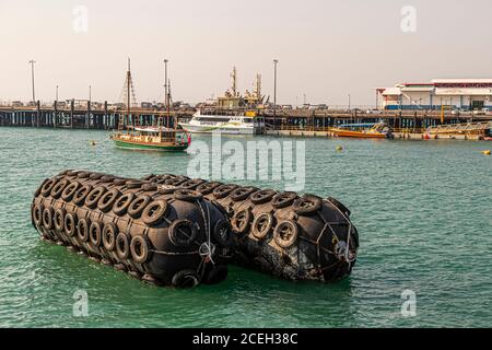 Riesige Bojen, die in Autoreifen eingewickelt sind, treiben im Hafen von Darwin, Northern Territory, Australien, während ein traditionelles Segelschiff und die Fähre "Spirit of Darwin" hinter ihnen am Kai festgemacht liegen. Stockfoto