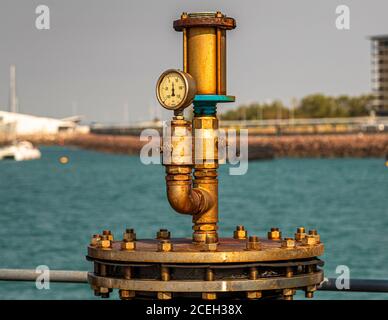 Ein Druckmessgerät ist auf einer Messingrohrarmatur im Hafen von Darwin, Northern Territory, Australien, montiert, wobei die Hafenbucht im Hintergrund unscharf ist. Stockfoto