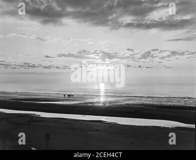 Schwarz-Weiß-Aufnahme von seichtem Wasser fließt auf strukturierten Sandstrand reflektierende Wolken in Himmel, Belgien. Stockfoto