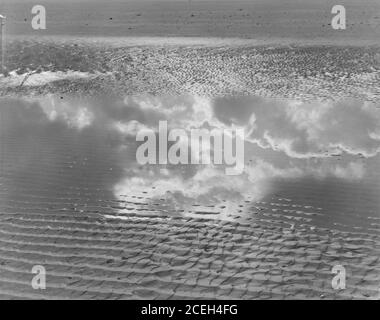 Schwarz-Weiß-Aufnahme von seichtem Wasser fließt auf strukturierten Sandstrand reflektierende Wolken in Himmel, Belgien. Stockfoto