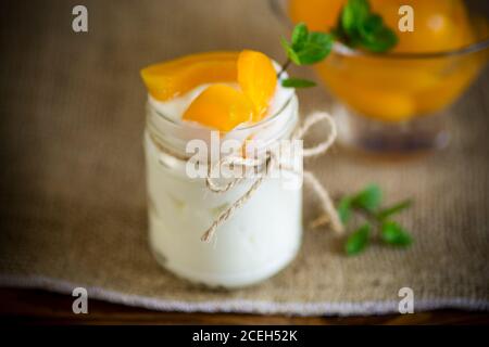 Hausgemachter süßer Joghurt mit Scheiben eingelegter Pfirsiche in einem Glasgefäß Stockfoto