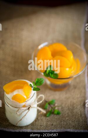 Hausgemachter süßer Joghurt mit Scheiben eingelegter Pfirsiche in einem Glasgefäß Stockfoto