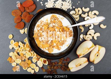 Müsli, Nüsse, Obst, Milch und Haferflocken zum Frühstück. Teller Haferflocken, Cashew, Äpfel und Samen für leckeres Frühstück auf dunklem Schiefer Tablett. Diet, Deto Stockfoto