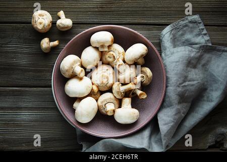 Frische Champignon-Pilze. Frische weiße Champignon Champignon in lila Schale auf Holz Hintergrund. Stockfoto