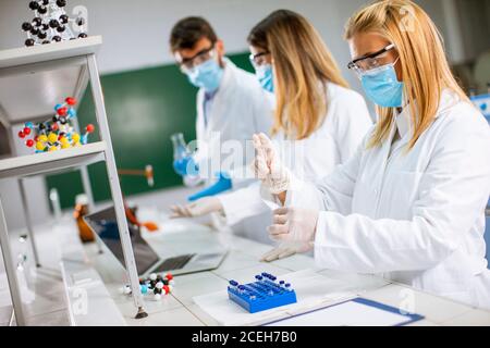 Frau Arzt trägt schützende Gesichtsmaske und Sicherheit googles in Labornadelspritze und Impfstoffflasche für Medikamentenfläschchen Stockfoto