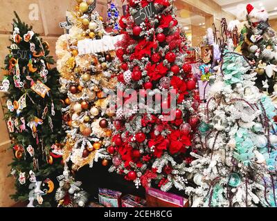 Bunte Weihnachtsbäume, geschmückt mit Kugeln, Blumen und Spielzeug in einem Schaufenster in einem Einkaufszentrum Stockfoto