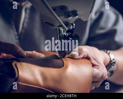 Unkenntlich Mann mit professioneller Maschine zu nähen Stück braun Leder für Schuhe Stockfoto