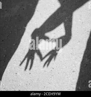 Zwei Hände bilden einen Herzschatten auf dem Asphalt. Schwarzweiß-Fotografie Stockfoto