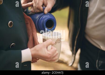 Ein Paar in der Liebe gießt Tee aus einer Thermoskanne in die tasse zum Aufwärmen auf der Straße Stockfoto