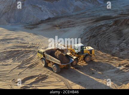 Radlader lädt Sand in schwere Bergbau-Muldenkipper im Tagebau. Schwere Maschinen im Tagebau, Bagger, Planierraupen und LKWs. Di Stockfoto