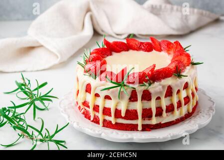 Hausgemachter roter Samtkuchen mit weißer Schokolade, frischen Erdbeeren und Rosmarin. Köstliches Gourmet-Dessert in einem weißen Teller auf einer Marmoroberfläche Stockfoto