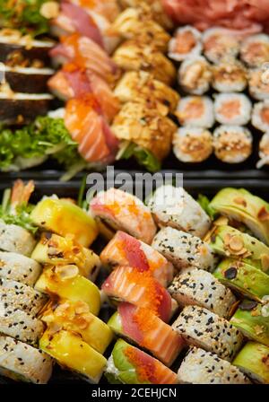 Nahaufnahme verschiedener Sushi-Sets in schwarzer Kunststoff-Lieferbox. Draufsicht Stockfoto