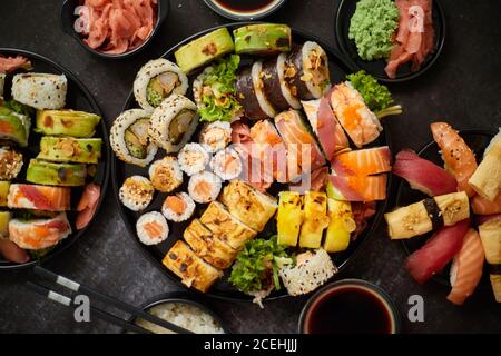 Asiatisches Essen. Menü Sushi mit Nigiri, Maki, Uramaki auf schwarzen Tellern. Verschiedene Arten von Sushi Stockfoto