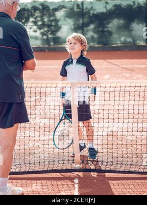 Zurück Ansicht Crop gealtertes Männchen und kleines Kind mit Tennis Schläger in der Nähe des Tennisnetzes auf dem Platz an sonnigen Tagen Stockfoto