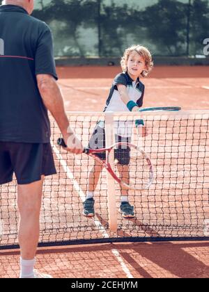 Zurück Ansicht Crop gealtertes Männchen und kleines Kind mit Tennis Schläger in der Nähe des Tennisnetzes auf dem Platz an sonnigen Tagen Stockfoto