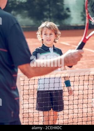 Zurück Ansicht Crop gealtertes Männchen und kleines Kind mit Tennis Schläger in der Nähe des Tennisnetzes auf dem Platz an sonnigen Tagen Stockfoto