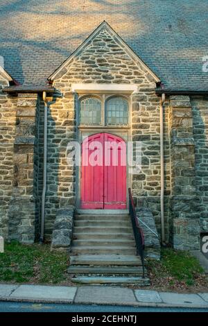 Eine helle rote Tür in einer gepflasterten Kirchenmauer mit Schritte, die zu ihm führen