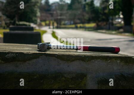 Ein Hammer mit einem roten und schwarzen Griff auf einem Kopfsteinpflaster Säule auf einer Suburban Street Stockfoto