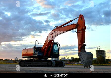 Große Raupenbagger auf einer Baustelle Hintergrund des atemberaubenden Sonnenuntergangs. Straßenreparatur, Asphaltersatz. Bagger der Graben Pipeline Graben. Stockfoto